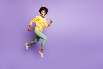 Fototapeta na wymiar Full length profile side photo of amazed funny crazy afro american girl jump run hurry autumn fall black friday bargain wear green sweater yellow pants trousers isolated violet color background