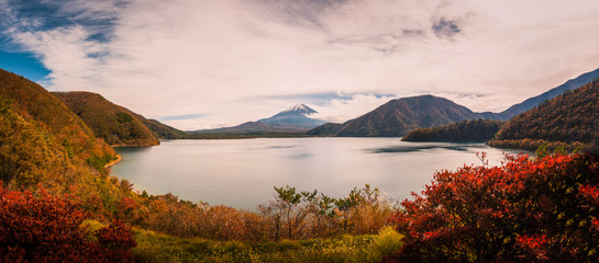 Landscape image of Mt. Fuji over Lake Motosu with autumn foliage at sunset in Yamanashi, Japan.
