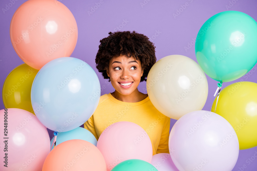 Wall mural Photo of charming cheerful cute nice enjoying black youngster wearing yellow sweater smiling toothily surrounded with balloons multicolor isolated over violet pastel color background