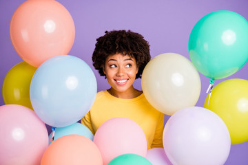 Fototapeta na wymiar Photo of charming cheerful cute nice enjoying black youngster wearing yellow sweater smiling toothily surrounded with balloons multicolor isolated over violet pastel color background