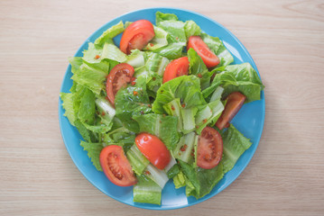 Delicious and healthy fresh organic tomato and romaine lettuce salad with vinaigrette dressing sauce on a wooden surface
