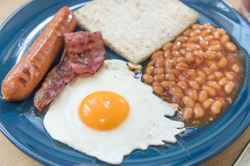 Full English breakfast with fried eggs, sausages, bacon, baked beans, toasts and mixed berry juice on a wooden surface