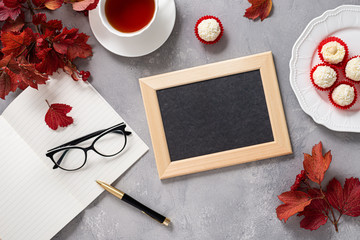 Teacher's day greeting card concept. Red autumn leaves, notebook, glasses, pen, tea, candies and black empty chalkboard with copy space on gray background.