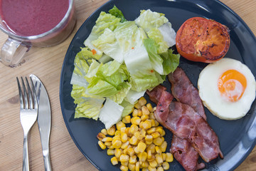 English breakfast with fried eggs, bacon, butter corn, grilled tomatoes and fresh salad with olive oil and vinegar sauce served with mixed berry juice