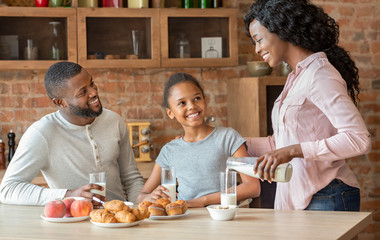Friendly family drinking milk, eating pastry together at kitchen