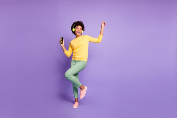 Fototapeta na wymiar Full length body size photo of trendy stylish cute free girlfriend wearing green pants trousers yellow sweater footwear in headphones listening to music dancing isolated violet pastel color background