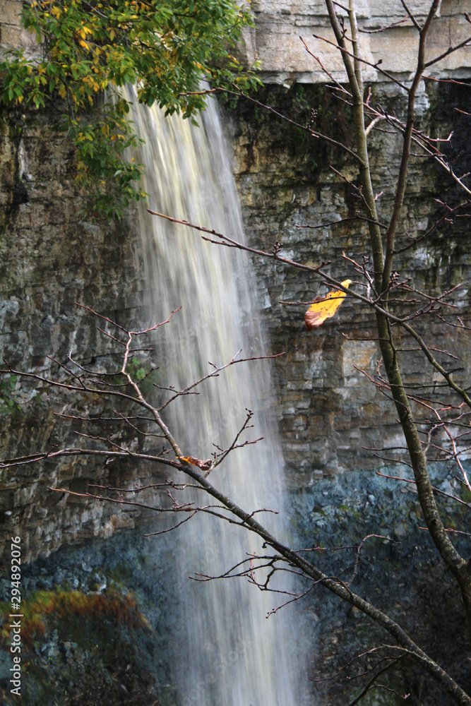 Wall mural large waterfall with high cliffs and trees with autumn foliage