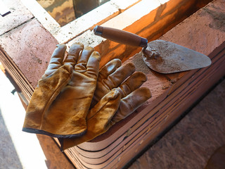 The stove’s working gauntlets lie on the edge of the red clay brick stove. Work gloves.