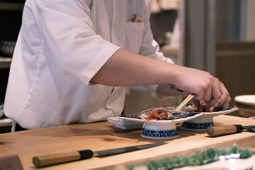 Fototapeta na wymiar Chef preparing sashimi dish at his counter, Omakase style Japanese traditional restaurant.