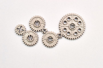 many plastic toy gear wheels connected to each other representing concept of team work and transmission on the paper background