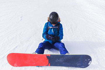 Sports background snowboard. Travel Lifestyle adventure concept, activities vacations outdoor in holidays. Snowboarder girl sitting on a slope. Snowboard close-up. Girl wears a helmet for protection.