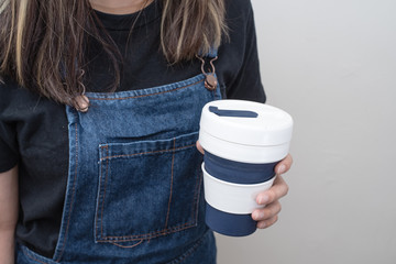 Young woman holding a silicone collapsible cup, reusable coffee tumbler.
