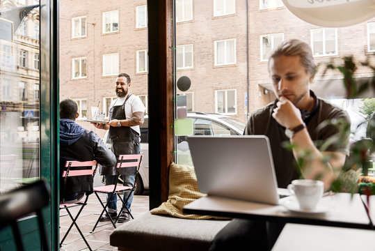 Barista serving young man at outdoor cafe table