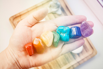 Woman hand sowing all seven color chakra crystal stones. Chakra energy flow healer concept. - obrazy, fototapety, plakaty