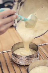 Woman's hands pouring cake batter into cake mold, ready to bake.