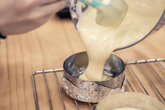 Woman's hands pouring cake batter into cake mold, ready to bake.