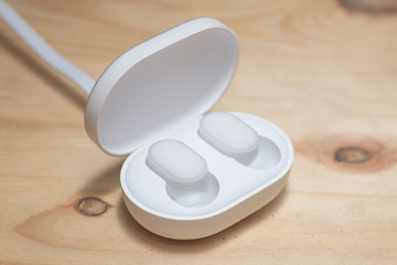 A pair of truly wireless earphones and charging carrying case on a wooden surface.