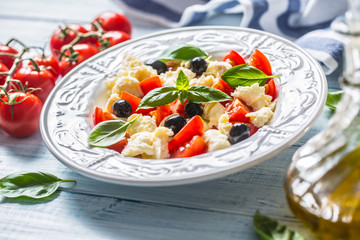 Caprese salad with mozzarella cheese fresh tomatoes olives and basil leaves. Italian or mediterranean healthy meal