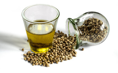 Hemp seeds in a jar and hempseed oil in a measuring glass beaker isolated on a white background.