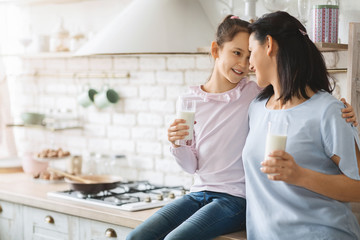 Young single mother and daughter drinking milk in kitchen together