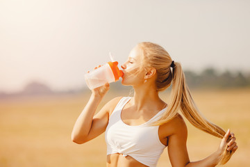 Beautiful blonde drinks water after yoga exercise in park from sports bottle