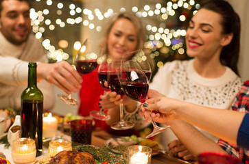 holidays and celebration concept - close up of happy friends having christmas dinner at home, drinking red wine and clinking glasses