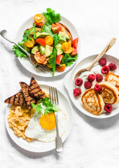 Savory and sweet breakfast - avocado, cherry tomatoes grilled  bread salad, fried egg with hummus and rye croutons and pancakes with greek yogurt and raspberries on light background, top view