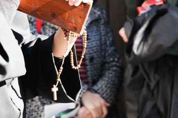 Rosario de madera con cruz colgado de la muñeca y mano cargando una cruz 
