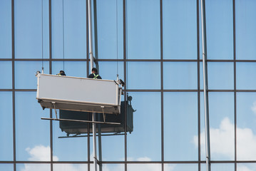 Asian window cleaners/workers on a suspended platform working on a glass facade in Hong Kong.