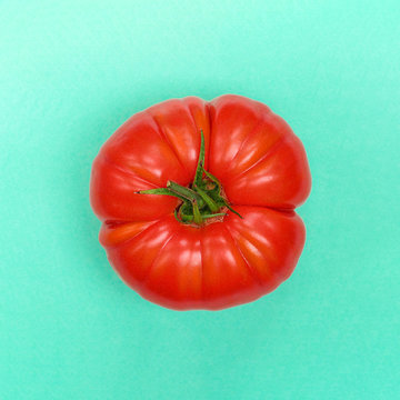 Homegrown organic beef tomato isolated on green background, top minimal view in natural light