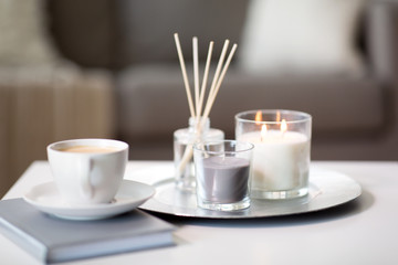 hygge and aromatherapy concept - coffee, candles and aroma reed diffuser on table at home