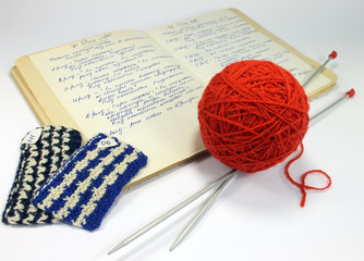 Old notebook with a description of knitting patterns, threads, knitting needles on a white table