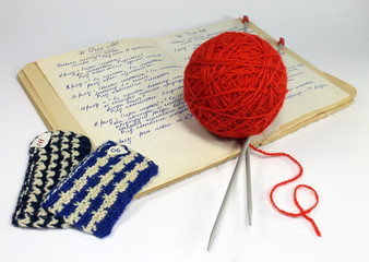 Old notebook with a description of knitting patterns, threads, knitting needles on a white table