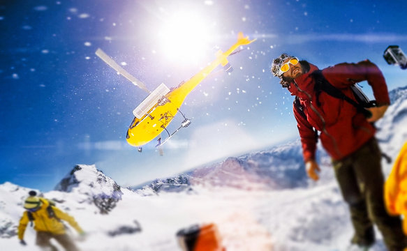 Actionsportlers were dropped by a helicopter at the top of the mountains while one person is taking a smile selfie with a wide angle camera.  The sun is shining brightly in the blue sky. There is a mo