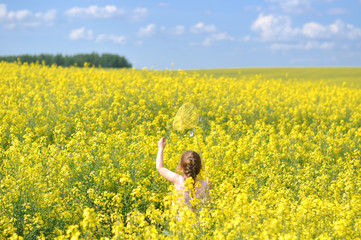 Little happy girl in a field of blooming yellow colza