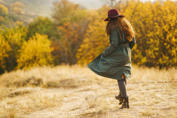 Beautiful young stylish girl in a coat walks in the autumn in the park. The girl is dressed in a green coat and a red hat. Beautiful evening. Autumn fashion. Lifestyle. High fashion portrait. 