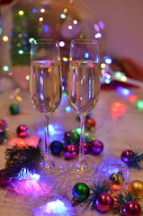 Glasses with champagne on a beautiful background of bright Christmas holiday lights. Christmas colorful toys for spruce. Photo with purple and yellow. 