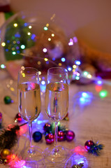Glasses with champagne on a beautiful background of bright Christmas holiday lights. Christmas colorful toys for spruce. Photo with purple and yellow. 