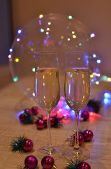 Glasses with champagne on a beautiful background of bright Christmas holiday lights. Christmas colorful toys for spruce. Photo with purple and yellow. 