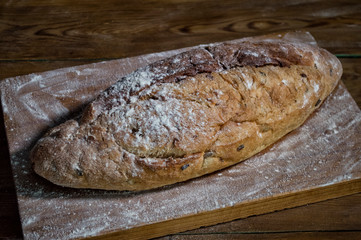 fresh bread on a kitchen board in flour. Wooden background, top view, closeup. Traditional bakery concept