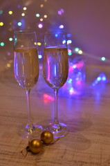 Glasses with champagne on a beautiful background of bright Christmas holiday lights. Christmas colorful toys for spruce. Photo with purple and yellow. 