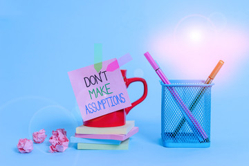 Word writing text Don T Make Assumptions. Business photo showcasing putting plan in future with percentage happening Cup pens holder note banners stacked pads paper balls pastel background