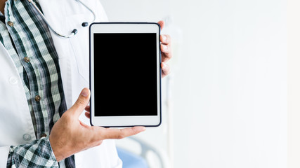 Close-up of man doctor therapeutic advising with positive emotions  holding up and showing digital tablet with a blank screen and bed in hospital background,copy space