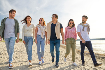 friendship, leisure and people concept - group of happy friends walking along beach in summer