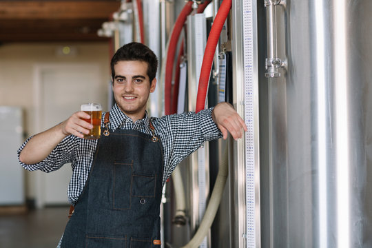 Portrait of confident young man holding beer glass at a brewery