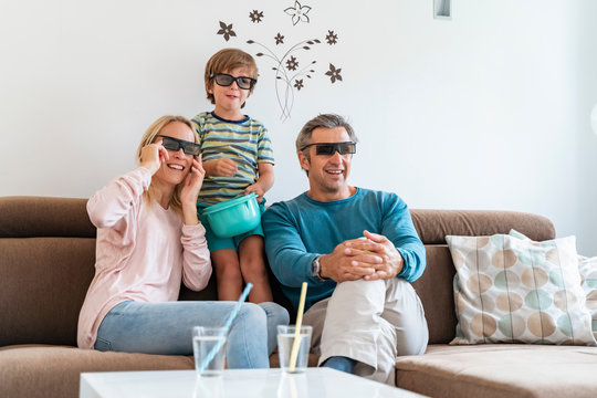 Father, mother and son wearing 3d glasses on couch at home watching Tv