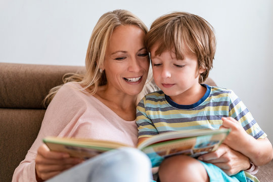 Mother and son reading a book together on couch at home
