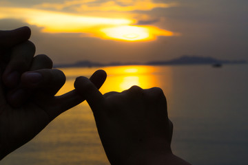 Silhouette of hand to pinky promise, pinky swear in front of the sun during sunset time. Love and...