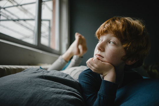 Portrait of boy looking out of window while lying on bed at home