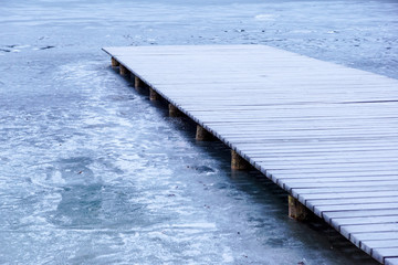 pier on the lake. Wooden bridge in forest in winter time with blue frozen lake. Lake for fishing with pier. Dark lake ice with hills